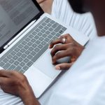 Close-up of a man using a laptop with a stylus pen for reading and working outdoors.