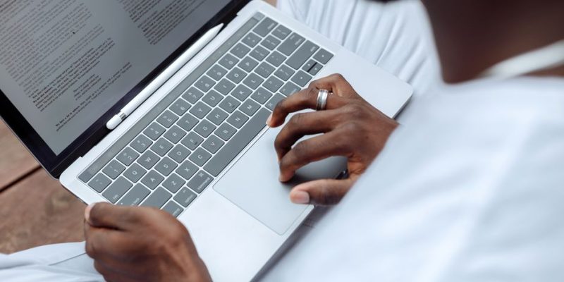 Close-up of a man using a laptop with a stylus pen for reading and working outdoors.